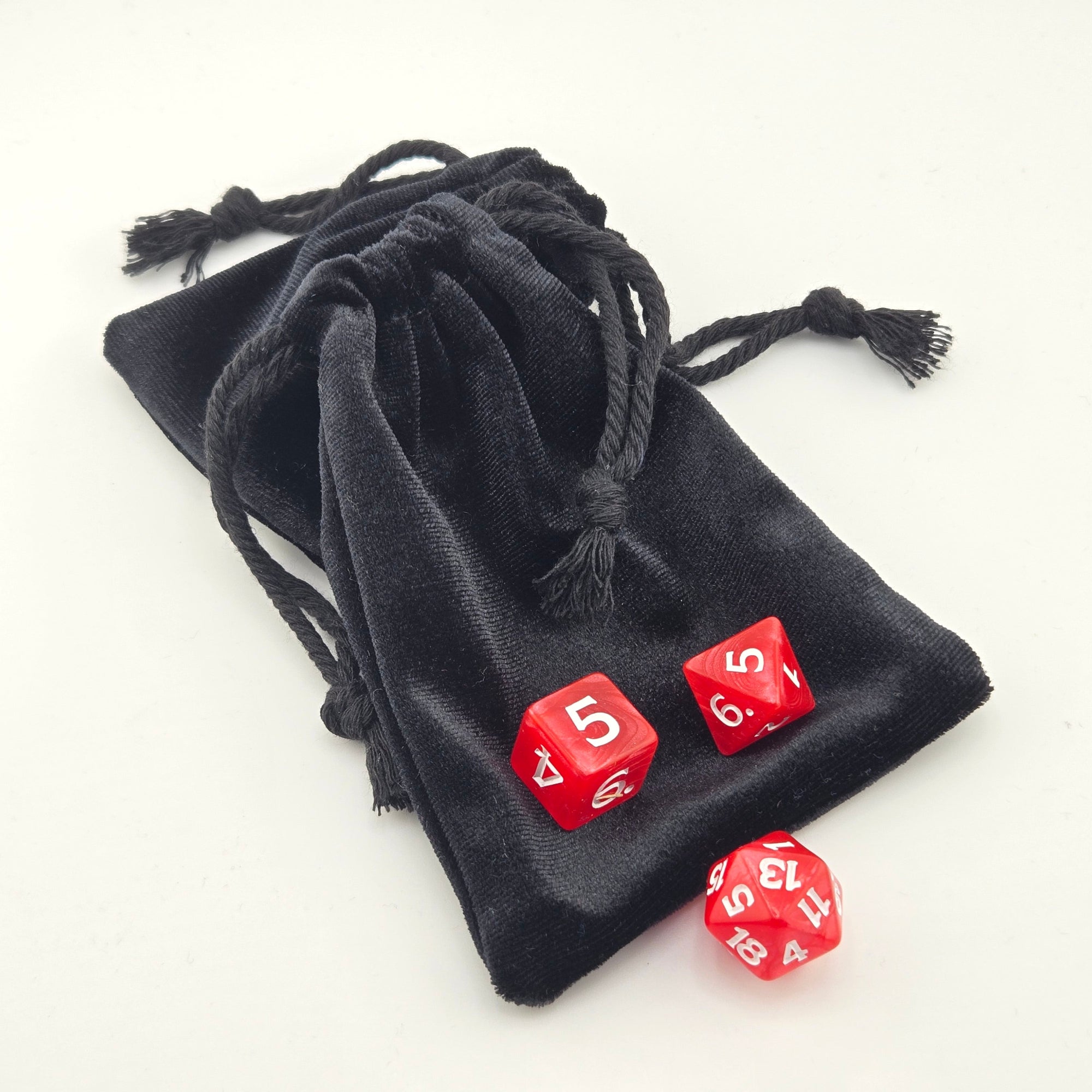 Glossy black drawstring bag on a white background with red dice typically used in a traditional dungeons and dragons set up.